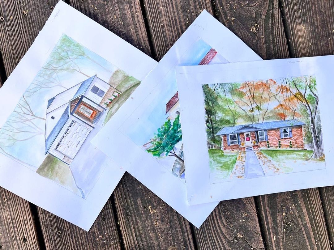 Three watercolor house portraits laid out on a wooden deck